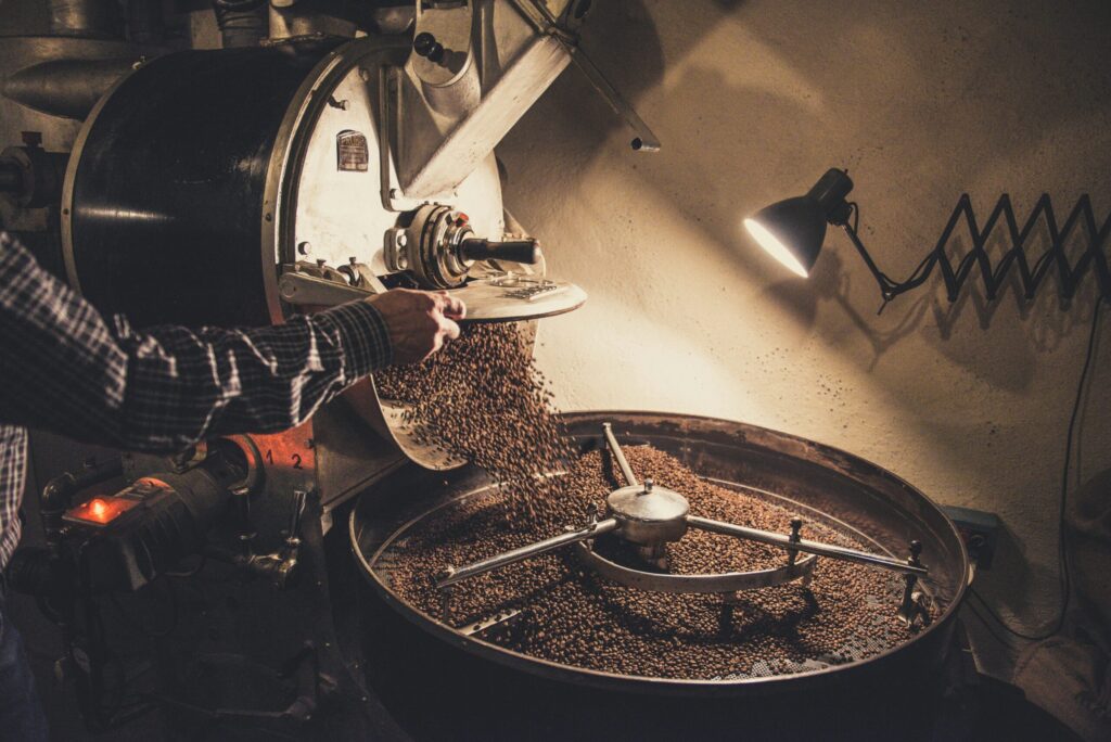 Galería 8 "Proceso de tueste de café en una tostadora industrial, donde un operario descarga los granos recién tostados en la bandeja de enfriamiento."